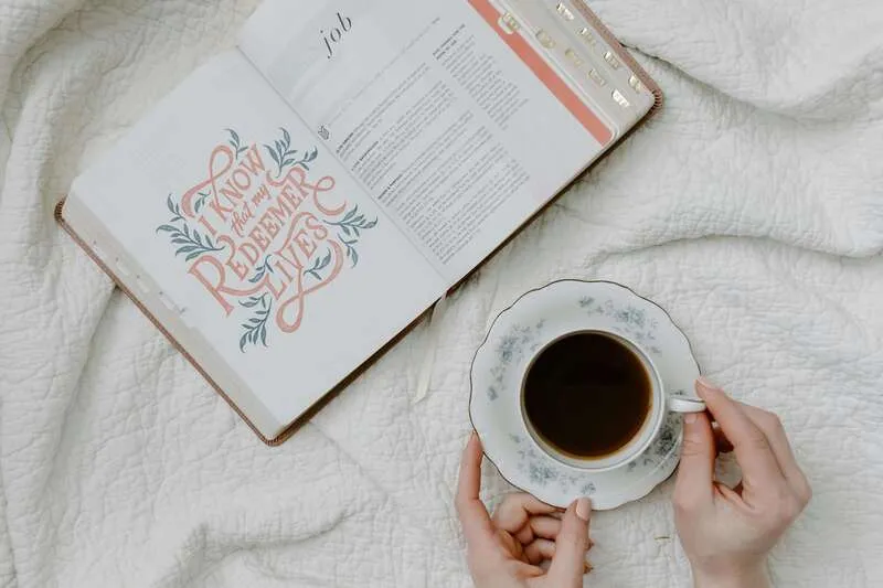 Imagem de uma xicara de café em cima de uma cama de colcha branca ao lado de uma bíblia, para exemplificar o post de melhores livros de ficção cristã