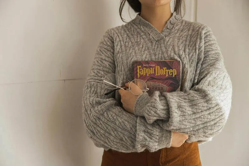 imagem de uma garota de moletom cinza sem mostrar o rossto ssegurando um livro de harry potter e de um oculos redondo para exemplificar o post de livros parecidos com harry potter